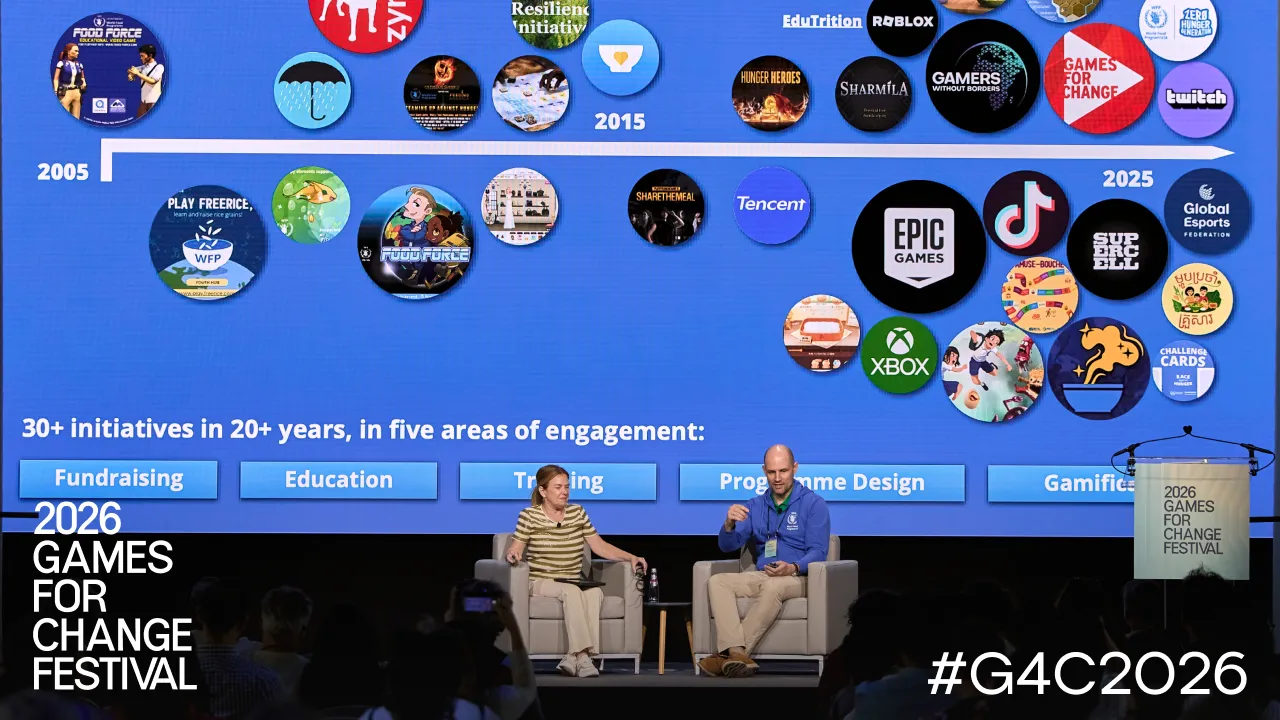Two speakers in conversation on stage at the 2026 Games for Change Festival, in front of a slide charting twenty years of initiatives.