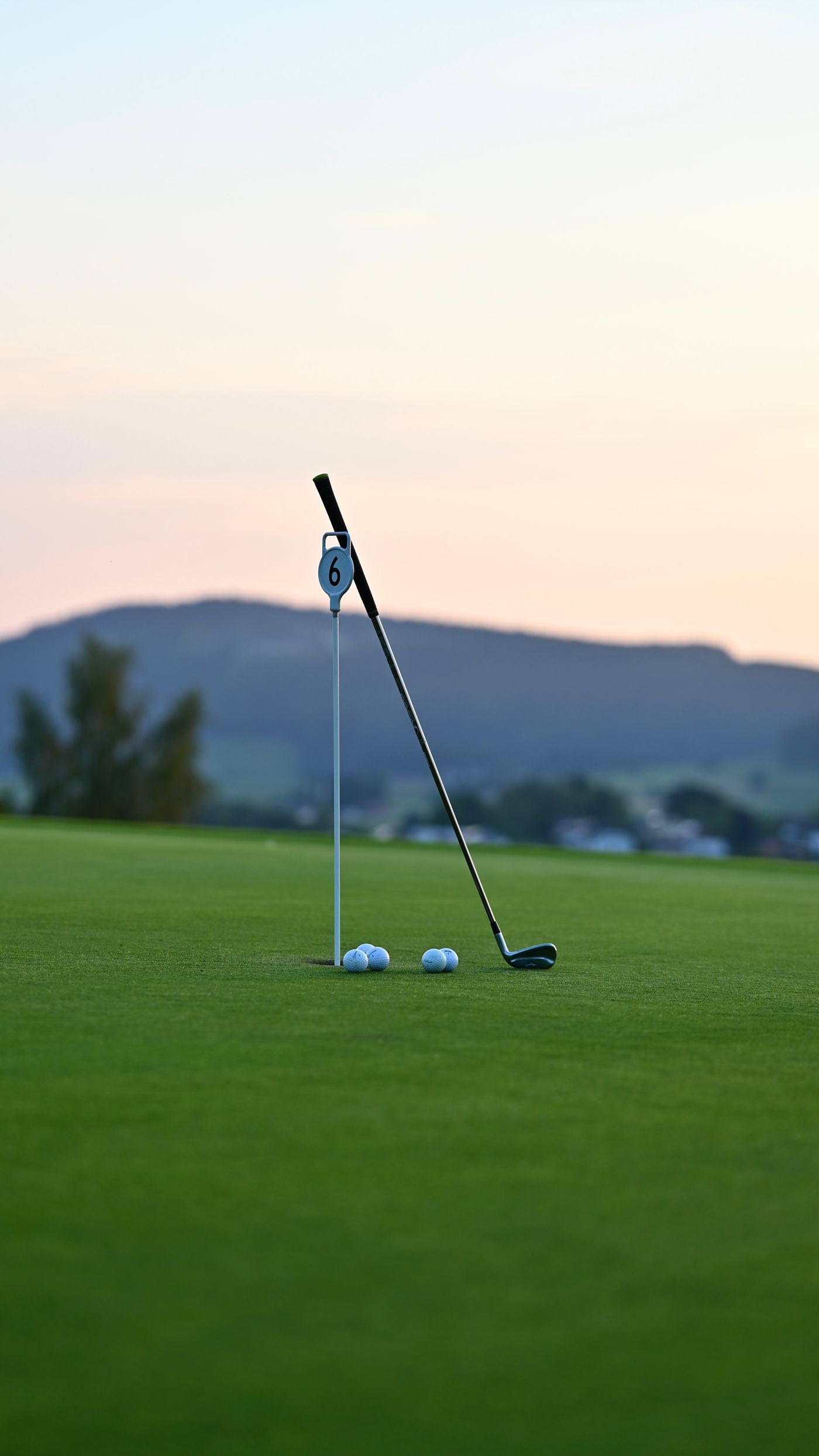 Golf club leaning on a numbered hole flag at sunset, with mountains in the background