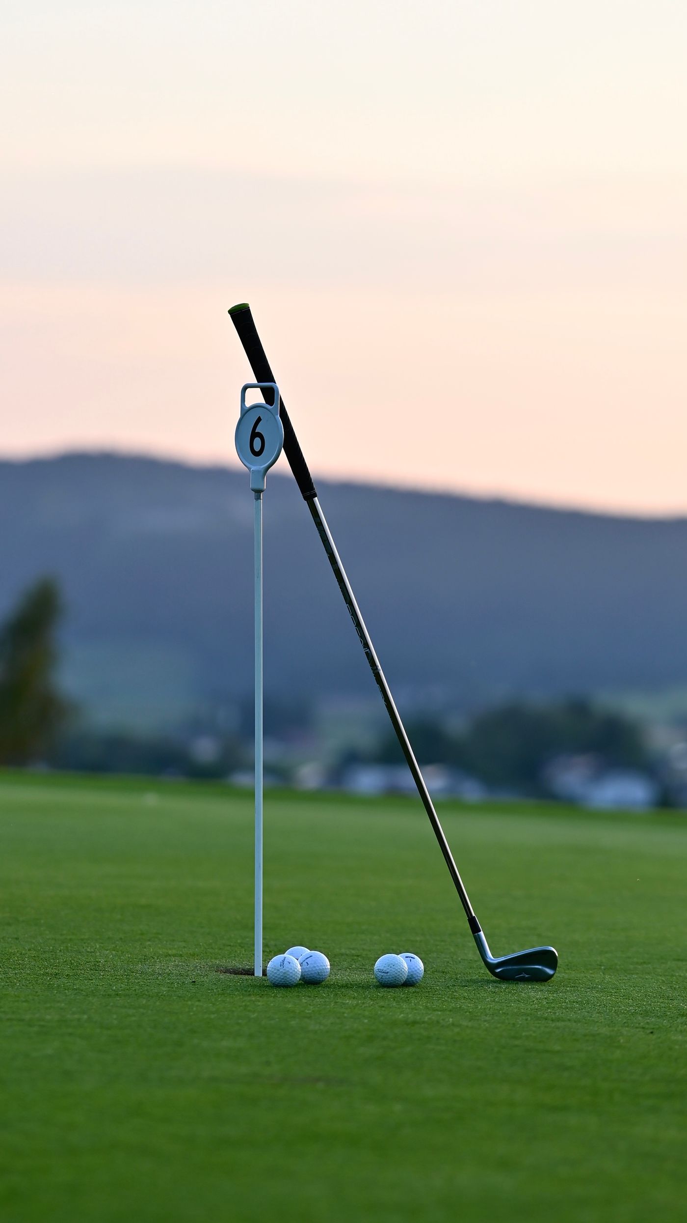Golf club leaning against a hole flag at dawn with misty mountains in the distance