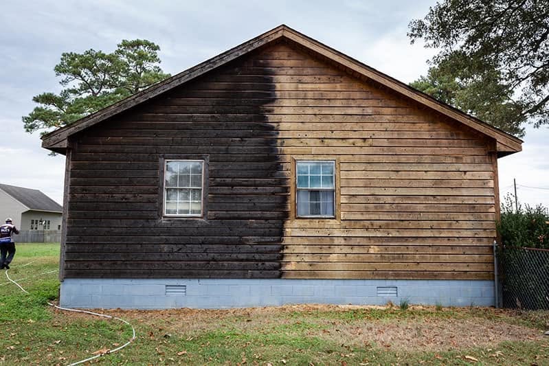 Log cabin cleaning in progress, with dark buildup on the left and cleaned wood on the right