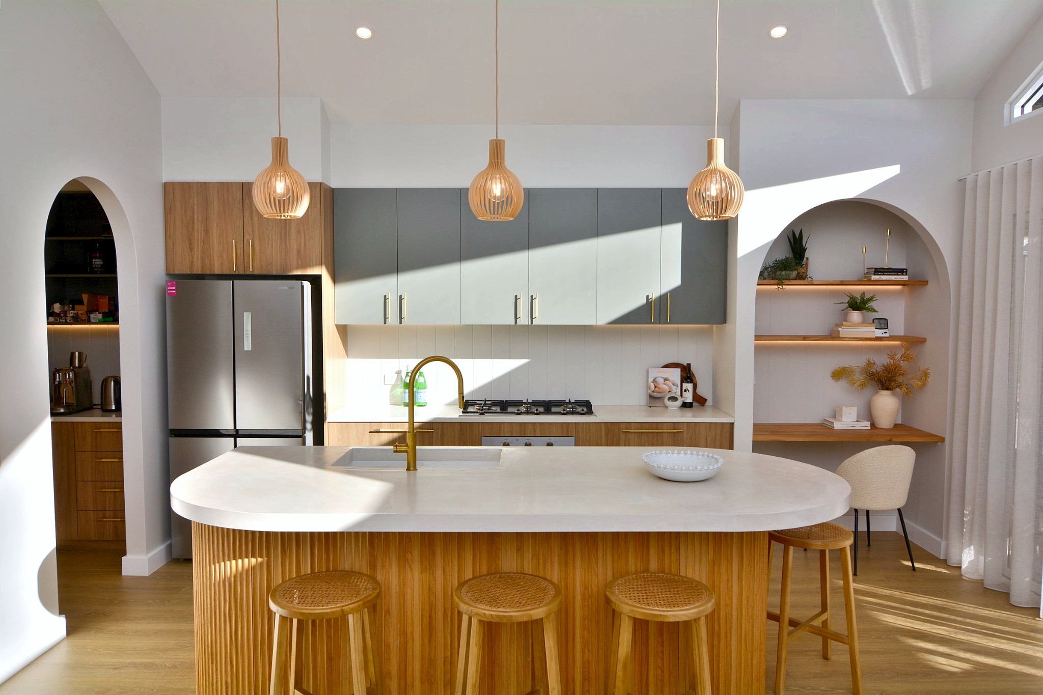 Kitchen with curved timber island, brass tap and arched pantry entry