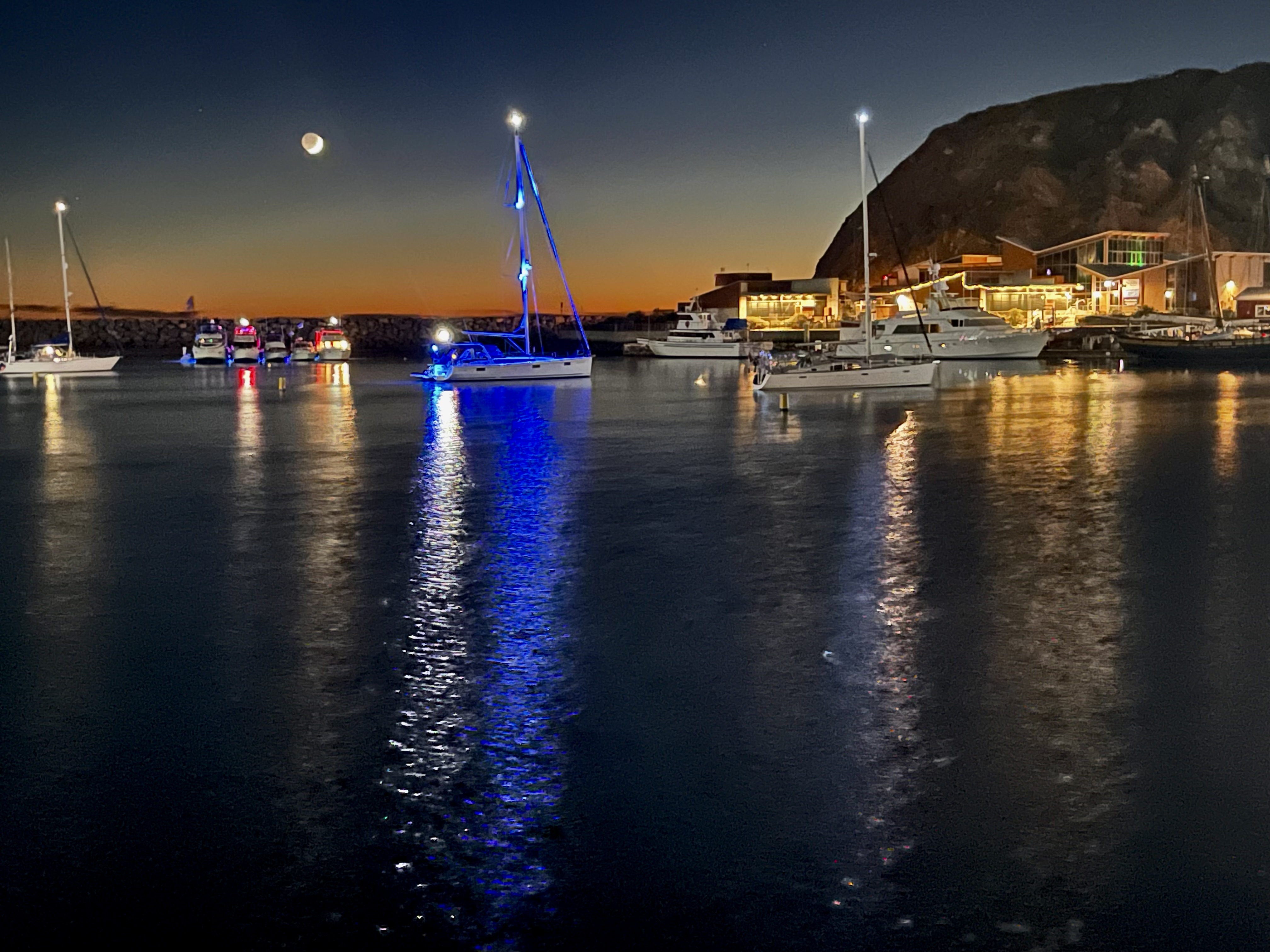 Harbor at dusk with sailboats lit up on calm water