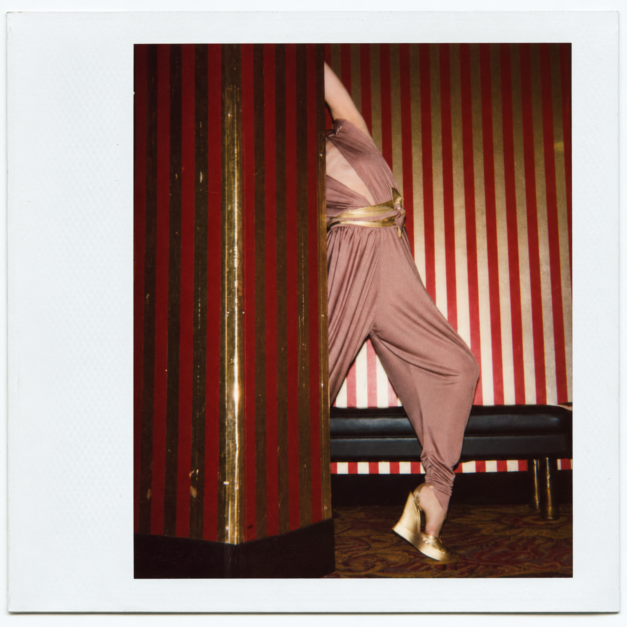 BODYAMR — Polaroid by Emma Summerton — dusty rose jumpsuit with gold accessories behind a striped partition