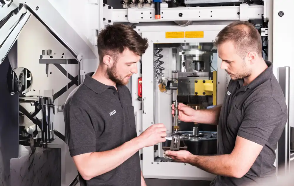 Zwei Felss-Techniker prüfen ein Bauteil an einer Fertigungsmaschine