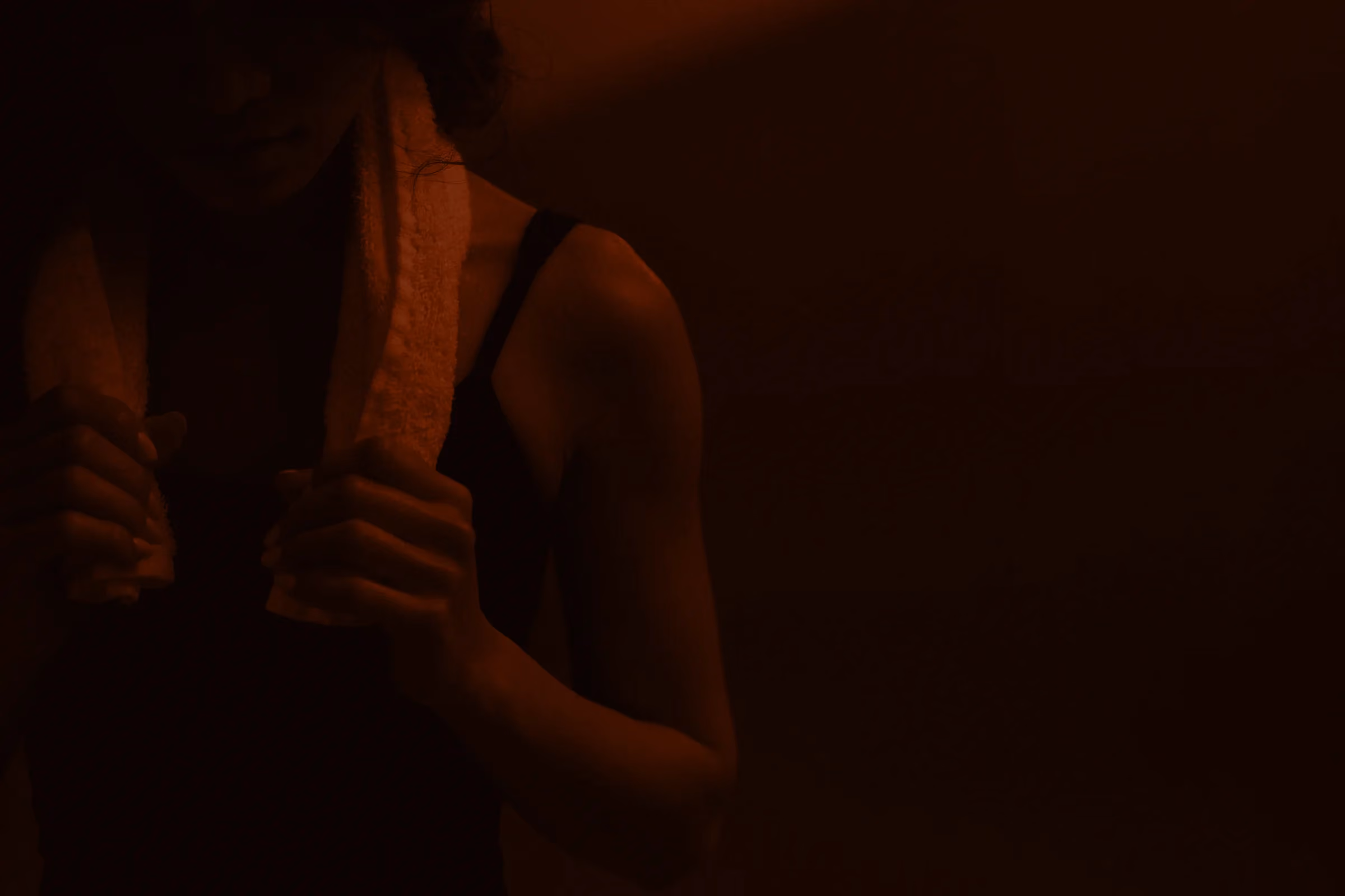 A member holding a towel around her neck in warm red light after class