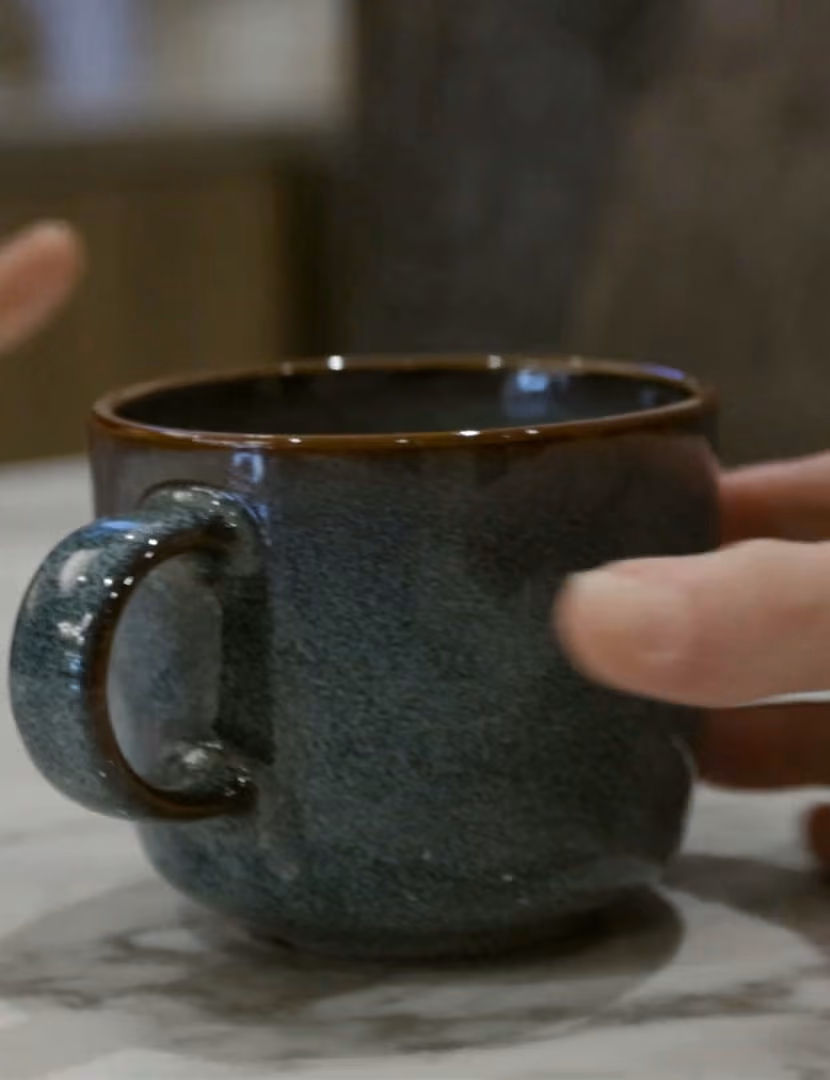 A hand around a stoneware espresso cup on the marble bar