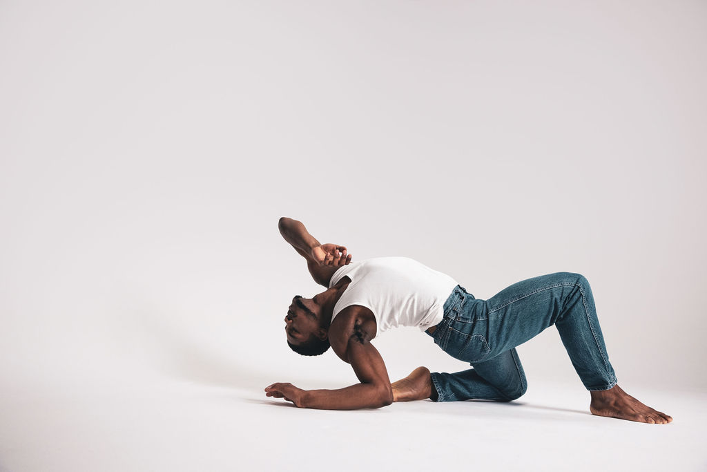 A dancer bridging up from the floor in a white tank and blue jeans, from the BNFTS studio shoot