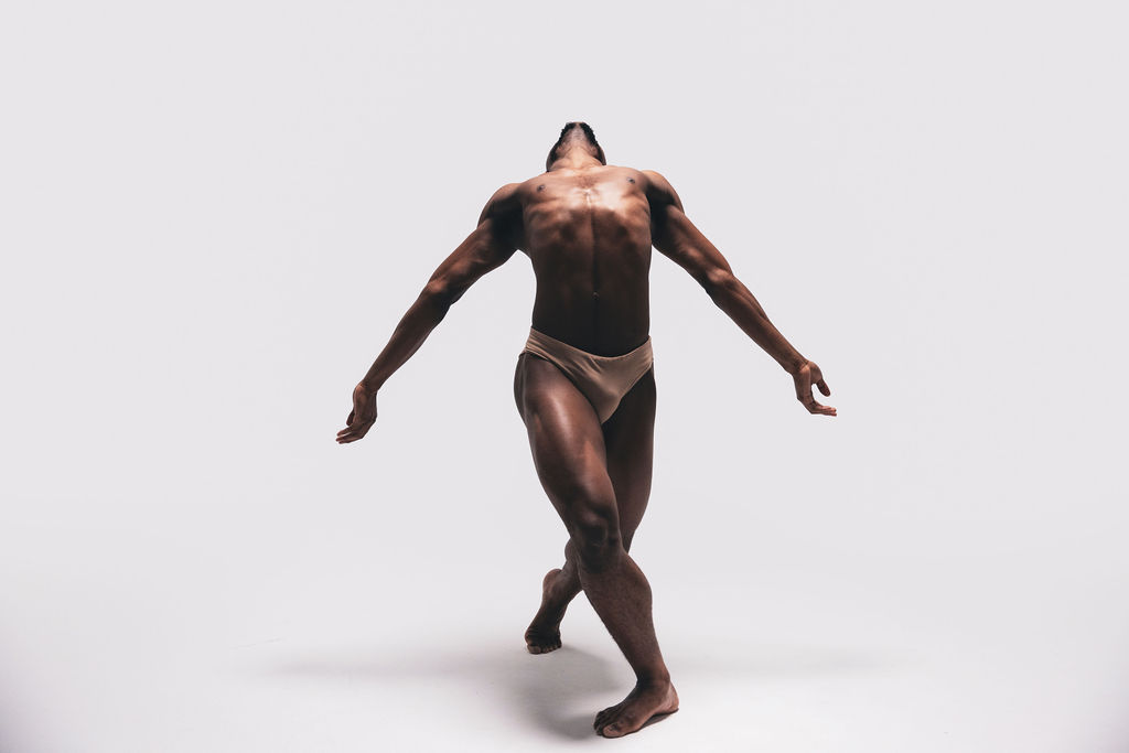 A near-nude dancer standing with their head tipped back and arms low and open, from the BNFTS Unbound campaign