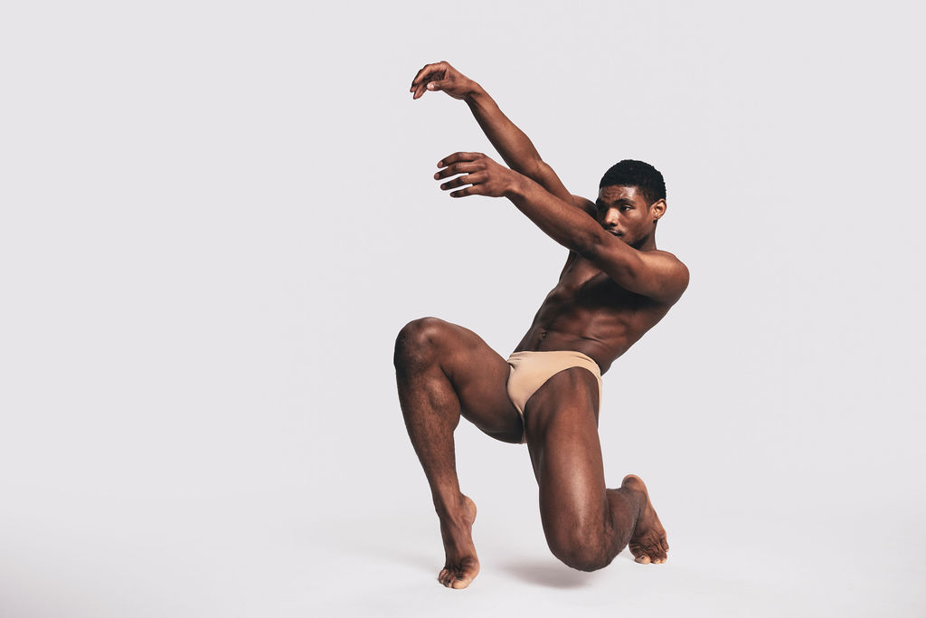 A near-nude dancer kneeling with one arm arched overhead, from the BNFTS Unbound campaign