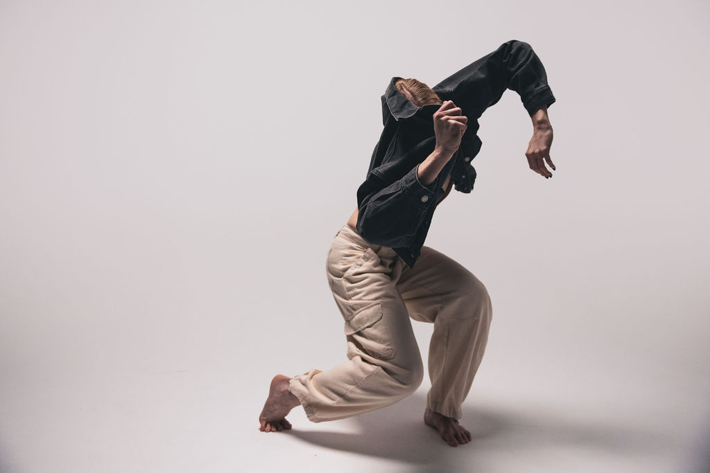 A dancer crouched low with their head down, in a black shirt and cream trousers, from the BNFTS studio shoot