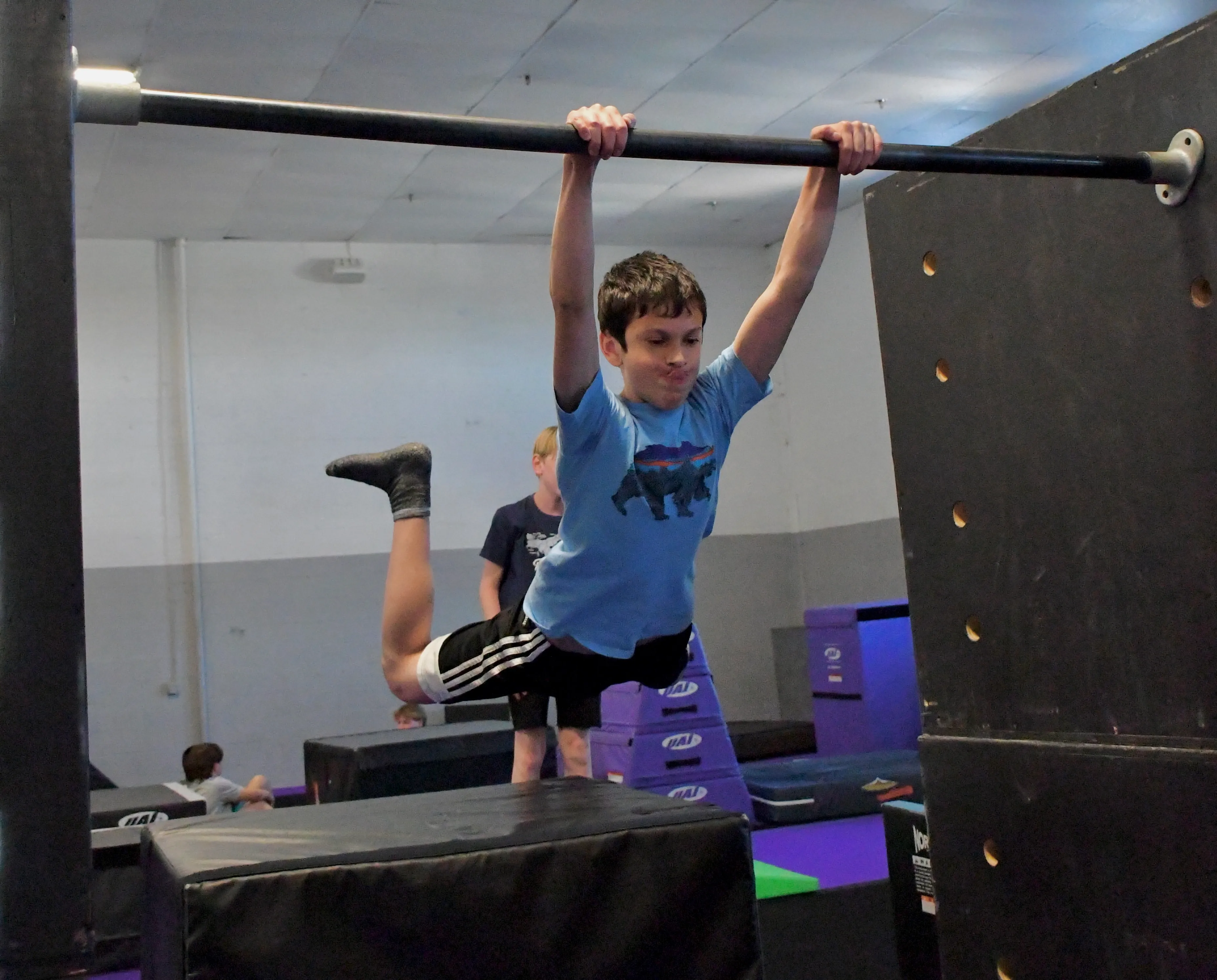 Smiling boy hanging from a bar at Bolt Parkour