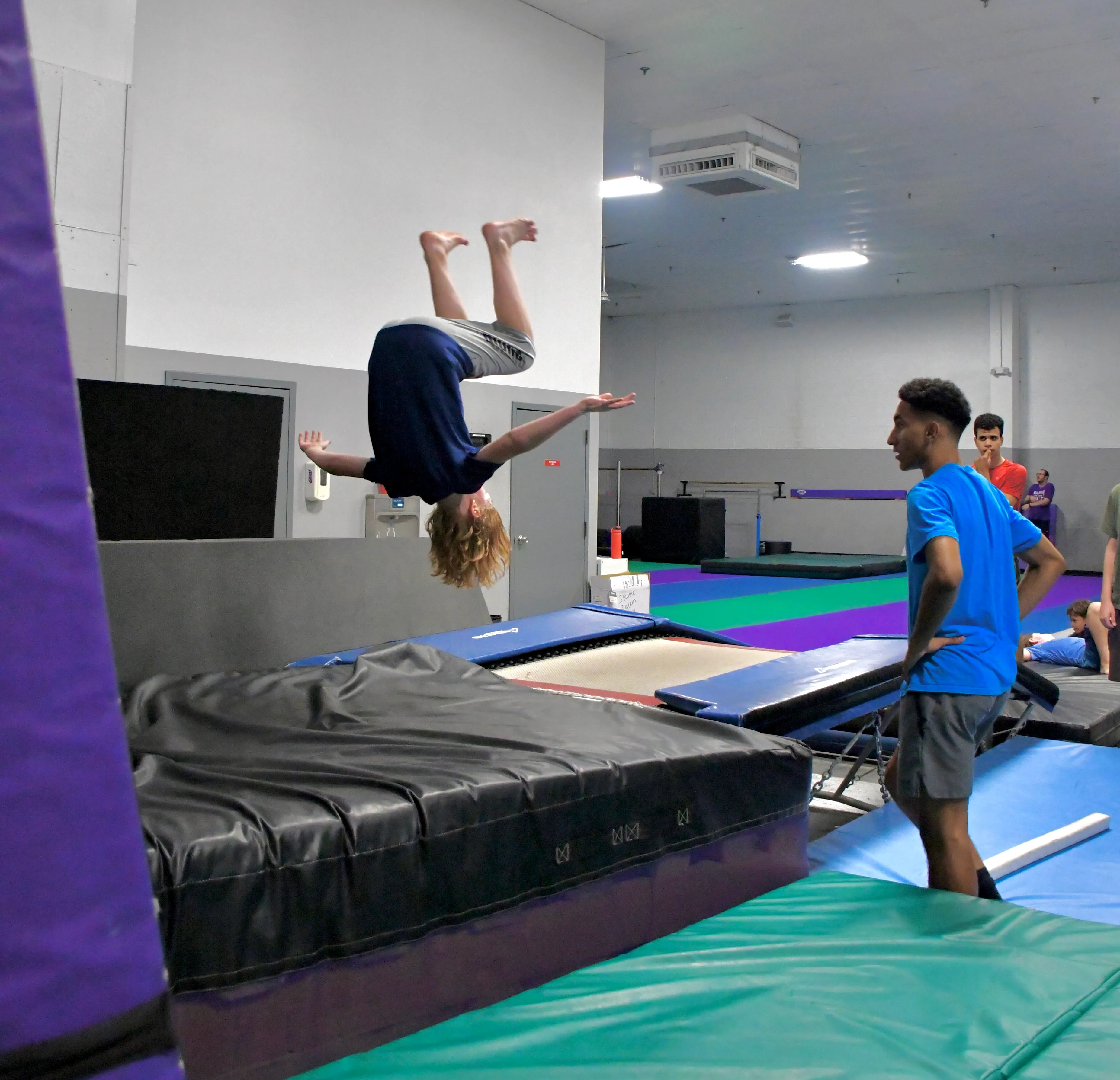 Student flipping onto a mat while a coach watches at Bolt Parkour