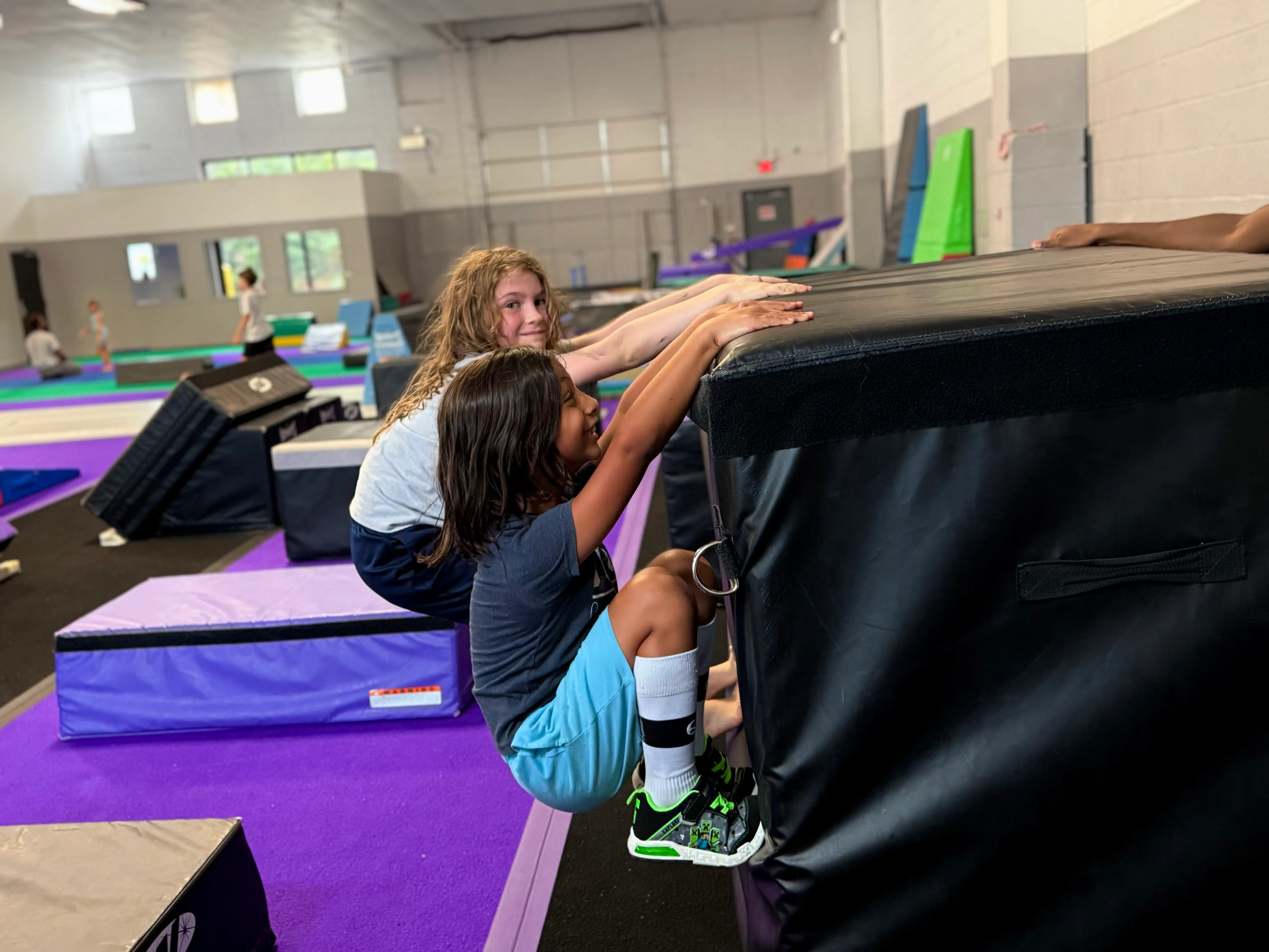 Two girls climbing a padded block at Bolt Parkour