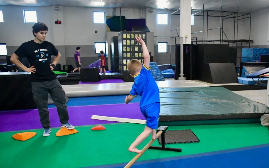 Coach guiding a young athlete across a balance rail