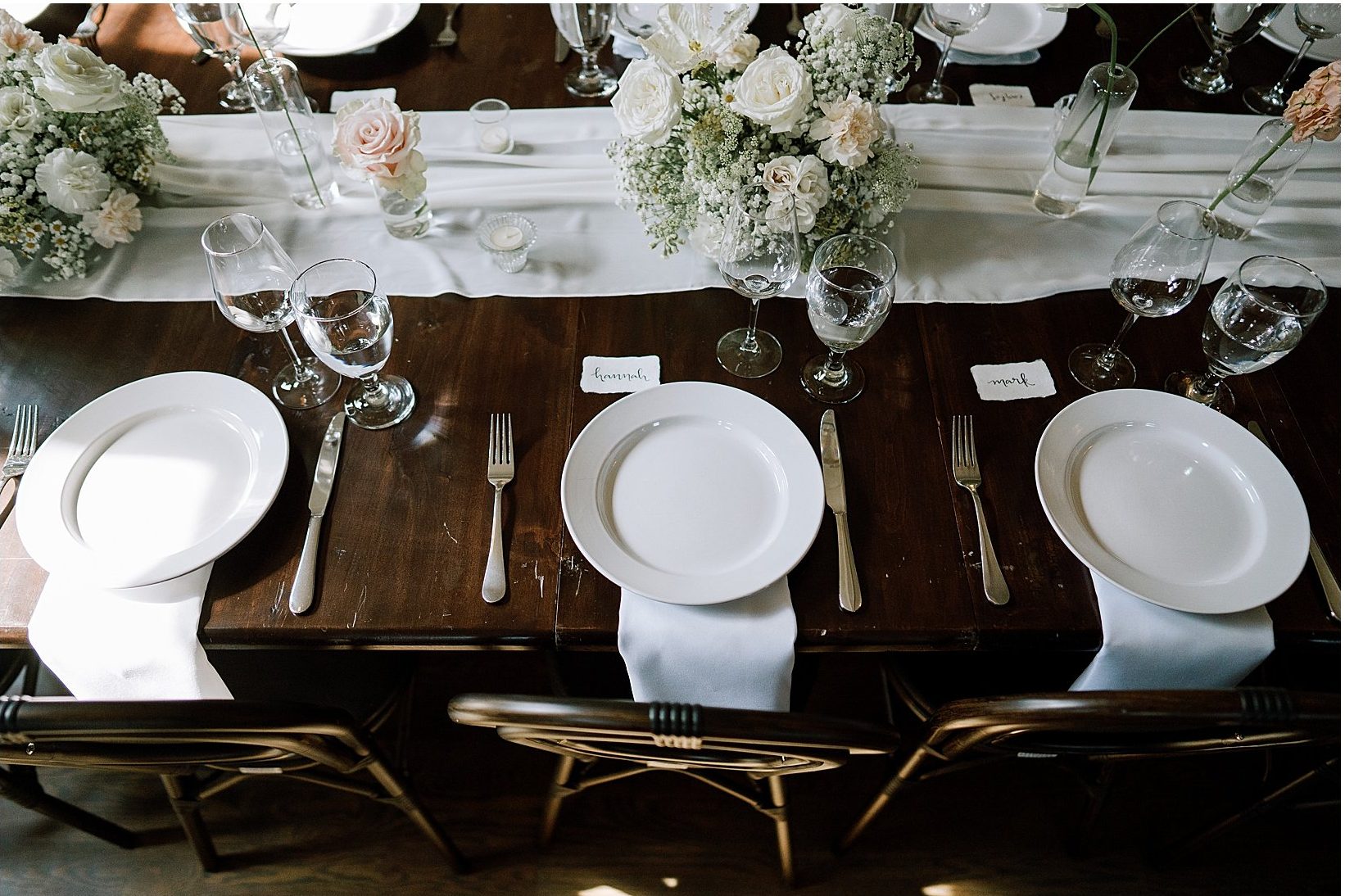 A long dark wood table set with white plates and flowers