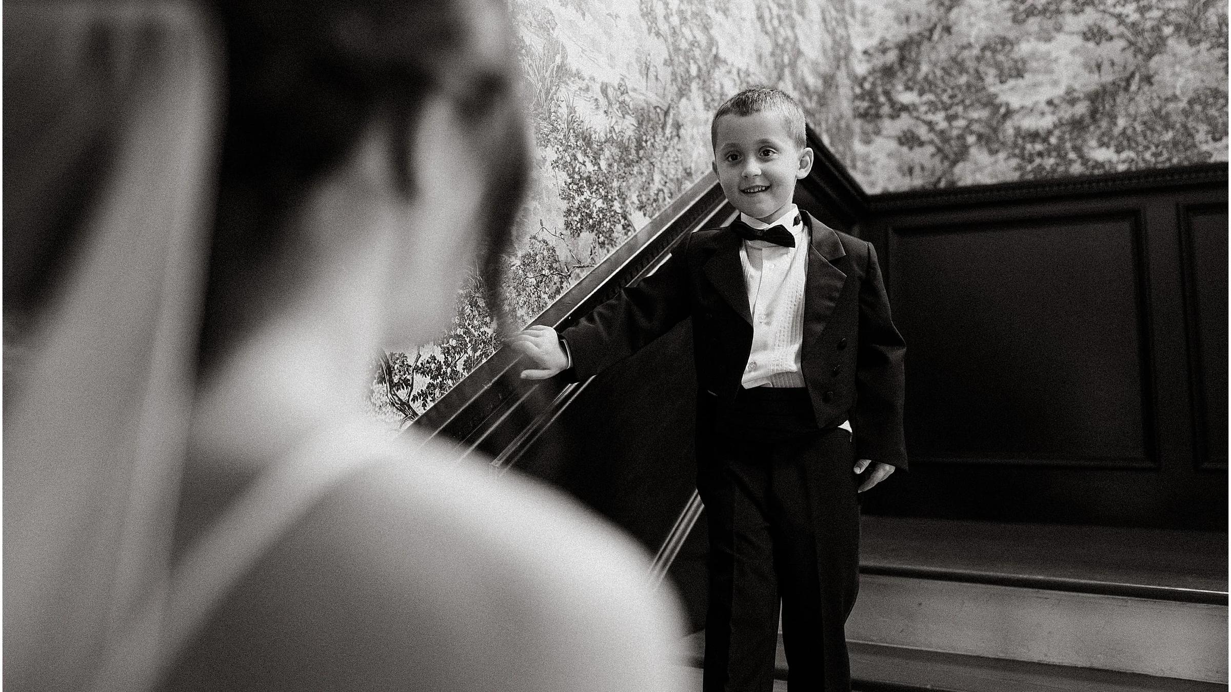 Black and white, a bride's veil blurred in front and a small boy on a dark staircase