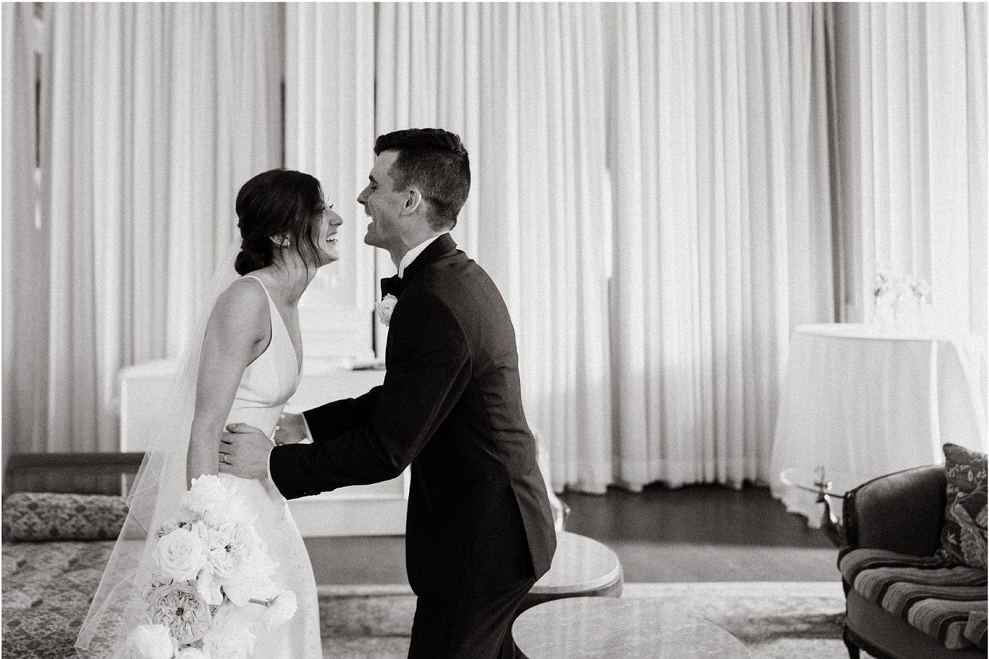 Black and white, the couple meeting at their first look beside tall curtains