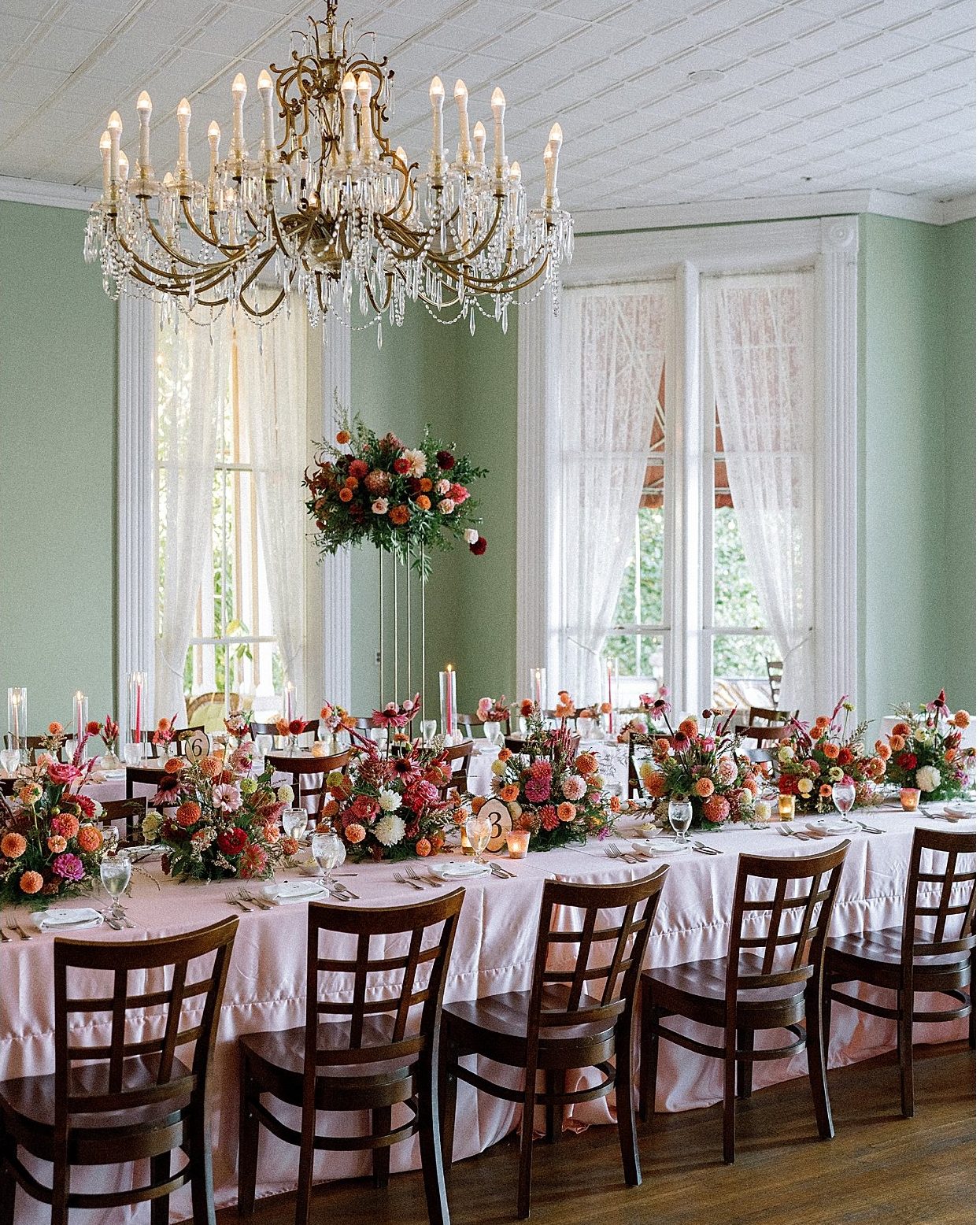 A dining room set for the wedding dinner beneath a chandelier.