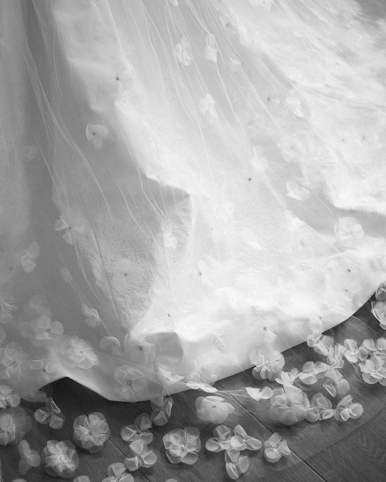 Black and white detail of a wedding dress hem with petals scattered on the floor