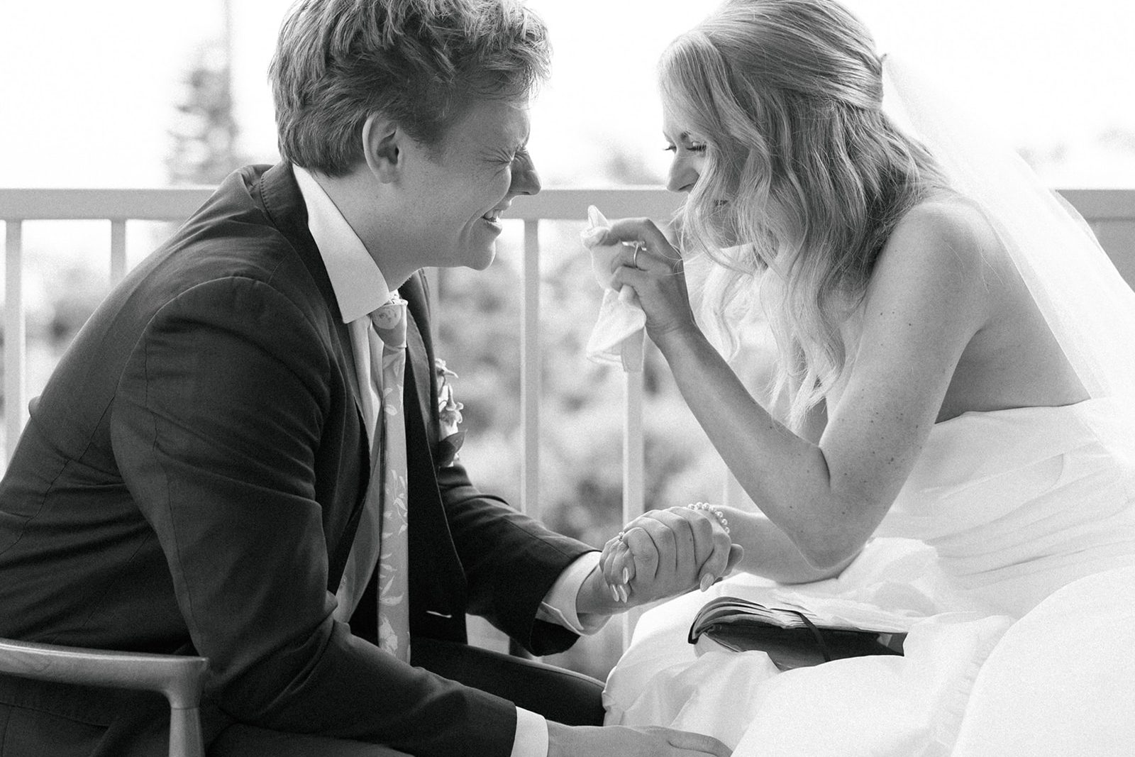 Black and white frame of the groom and bride laughing and wiping tears on a balcony
