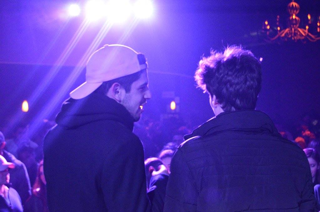 Two performers facing a crowd under purple stage lights