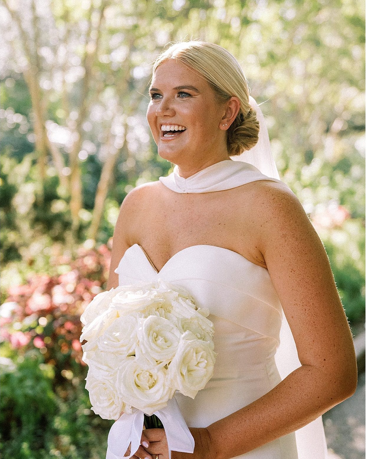 A close, backlit portrait of the bride laughing in a garden
