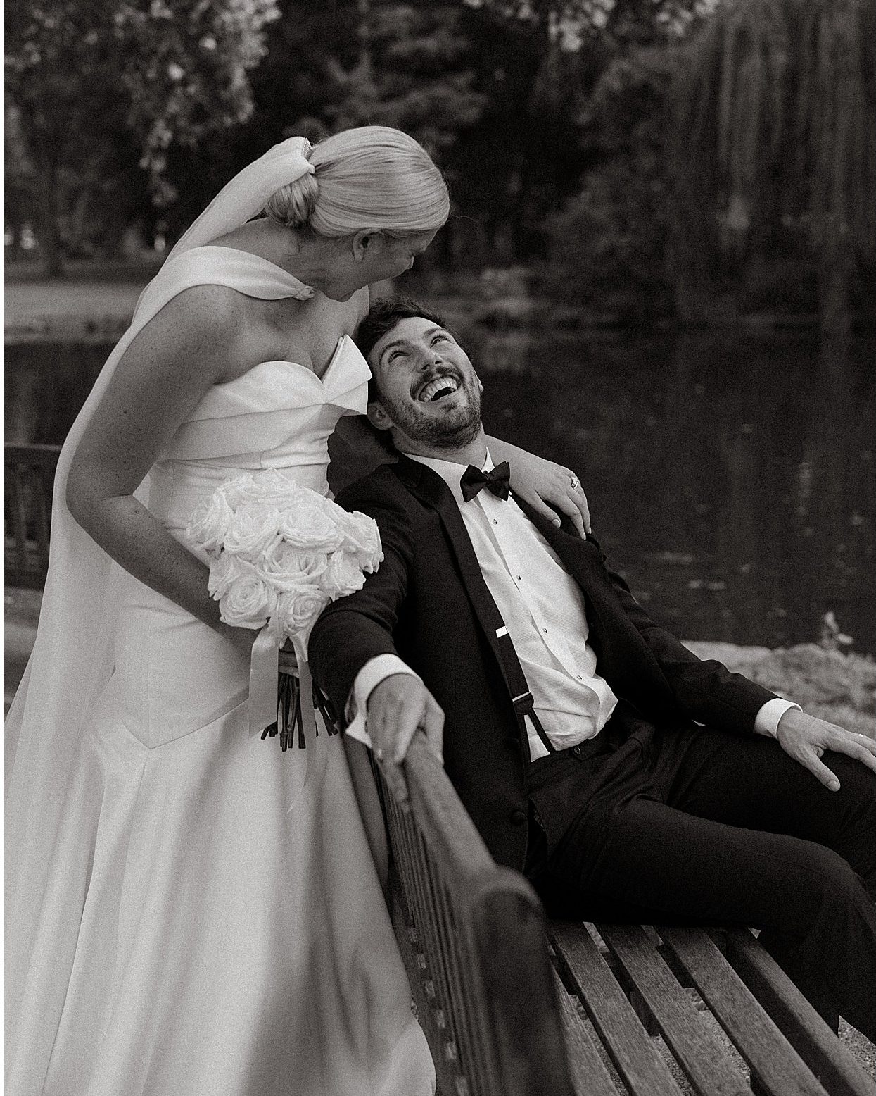 Black and white, the bride leaning over the laughing groom on a bench