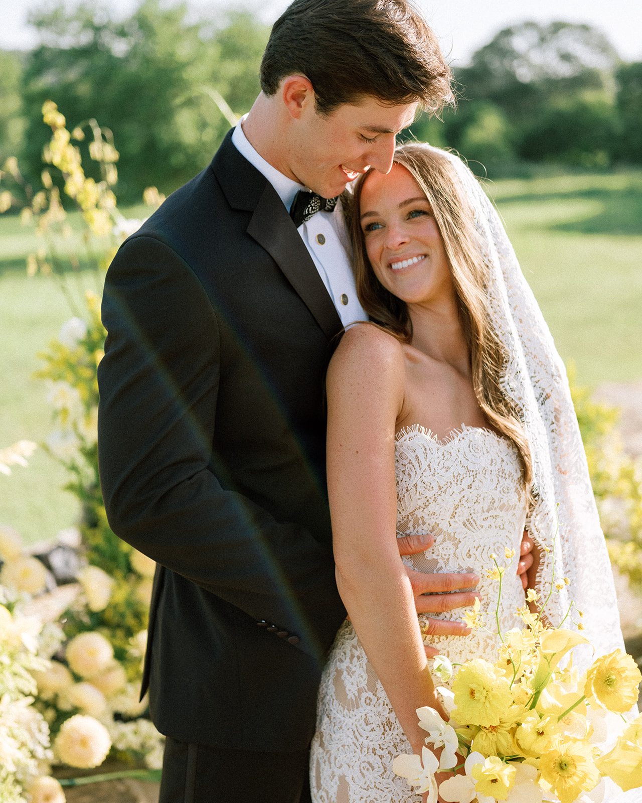The groom rests his forehead against the bride's, her bouquet of yellow flowers in front