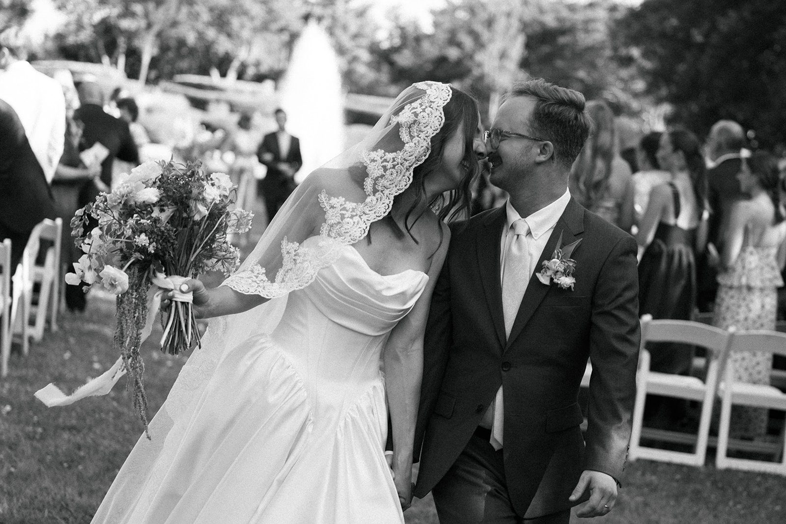Black and white frame of the couple walking together, the bride's veil lifted by the wind