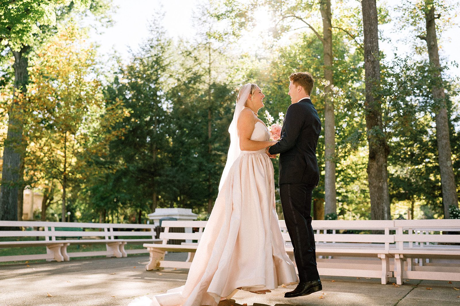 The couple face each other in the open air among autumn trees, the bride in a blush gown