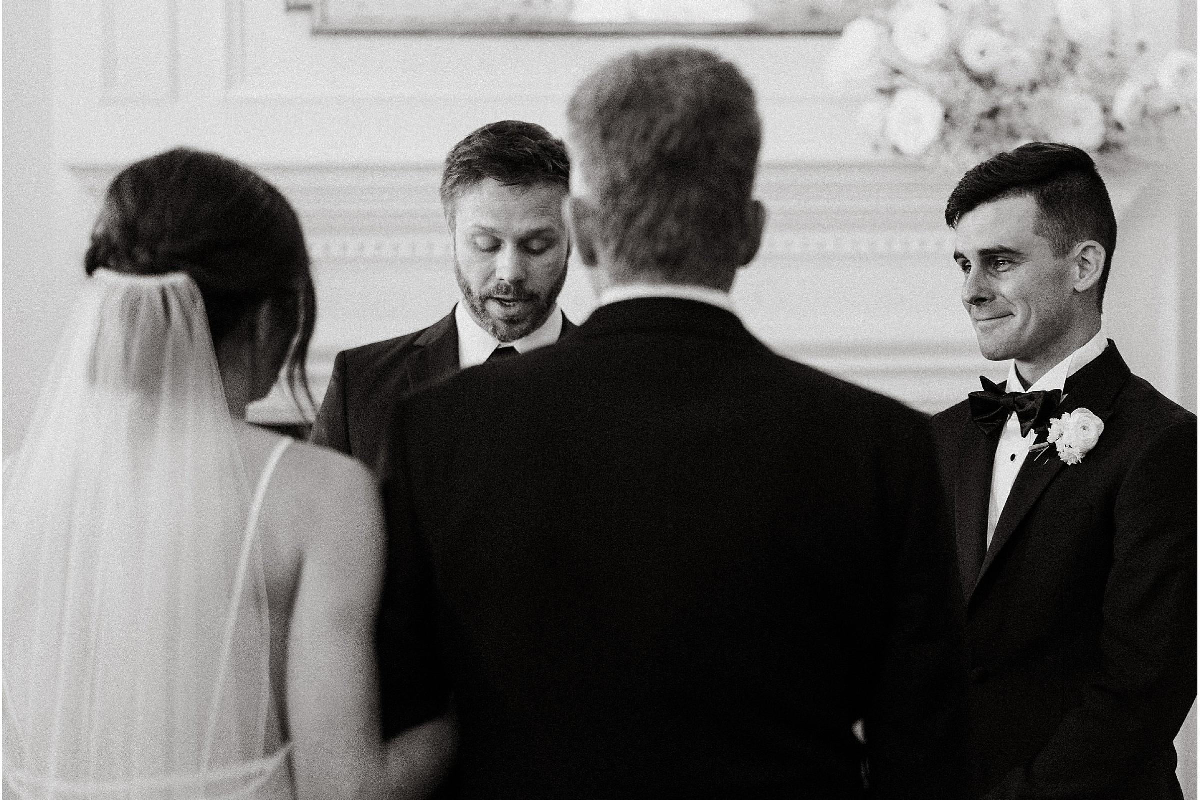 Black and white ceremony, the groom smiling over the officiant's shoulder