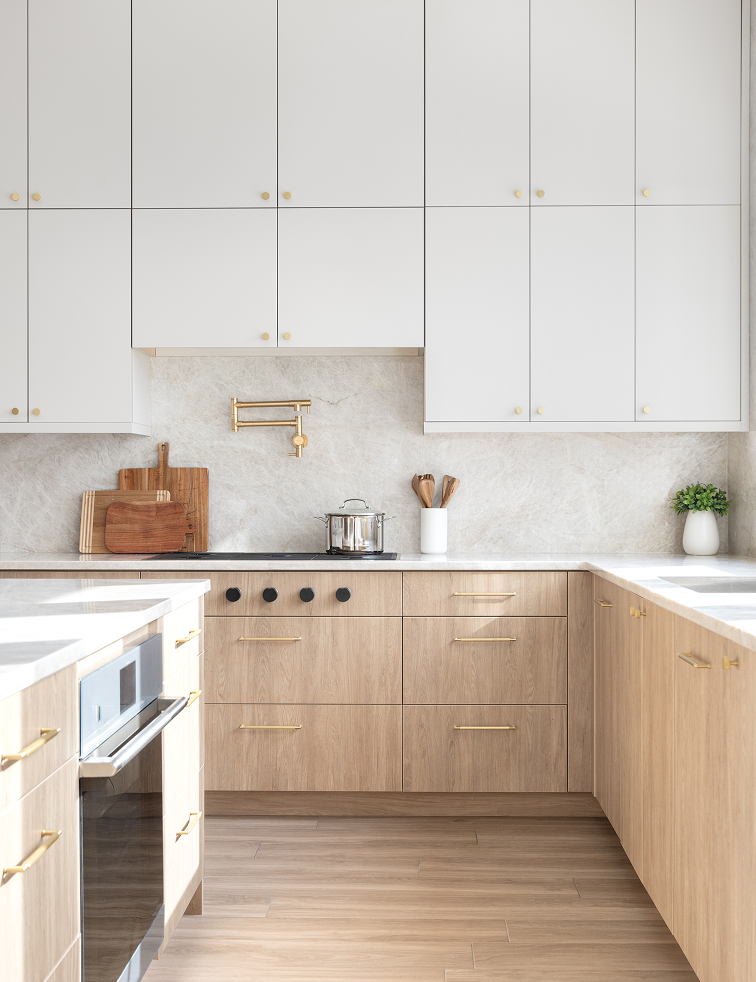 Modern kitchen with light wood lower cabinets, white upper cabinets, gold handles, and a stainless steel pot on the stove.
