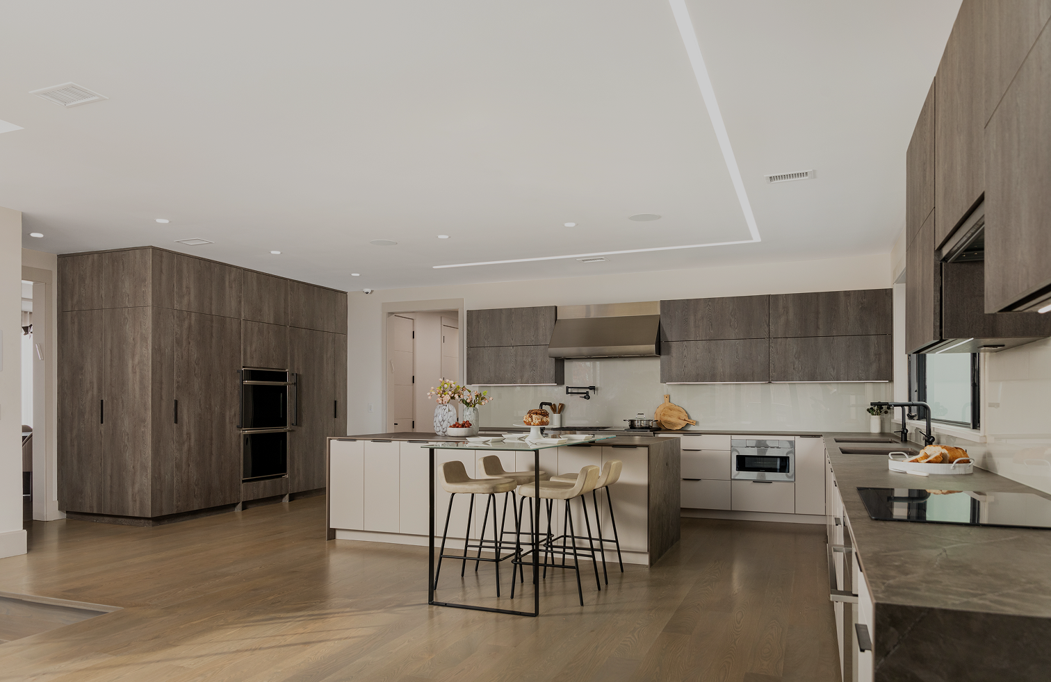 Modern kitchen with wood floor, gray upper cabinets, white lower cabinets, central island with bar stools.