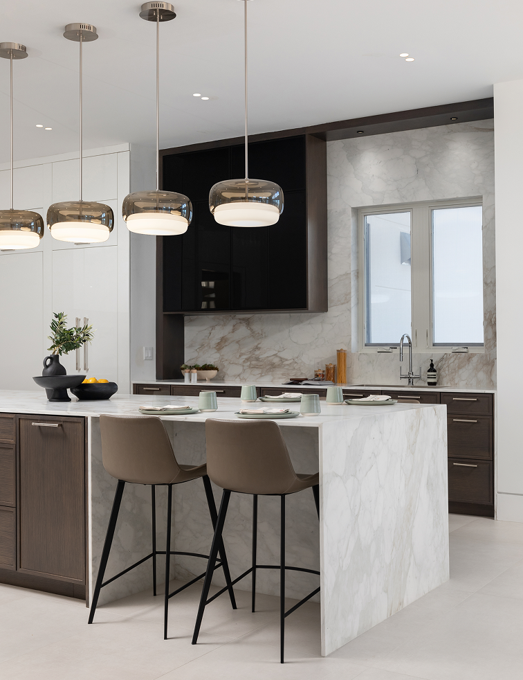 Modern kitchen with white marble island, two brown bar stools, hanging pendant lights, and dark wood cabinets.