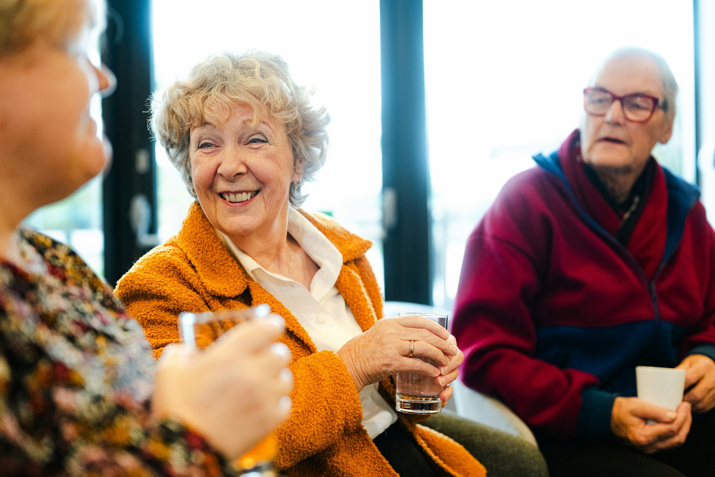Three older adults talking and smiling together in a community lounge