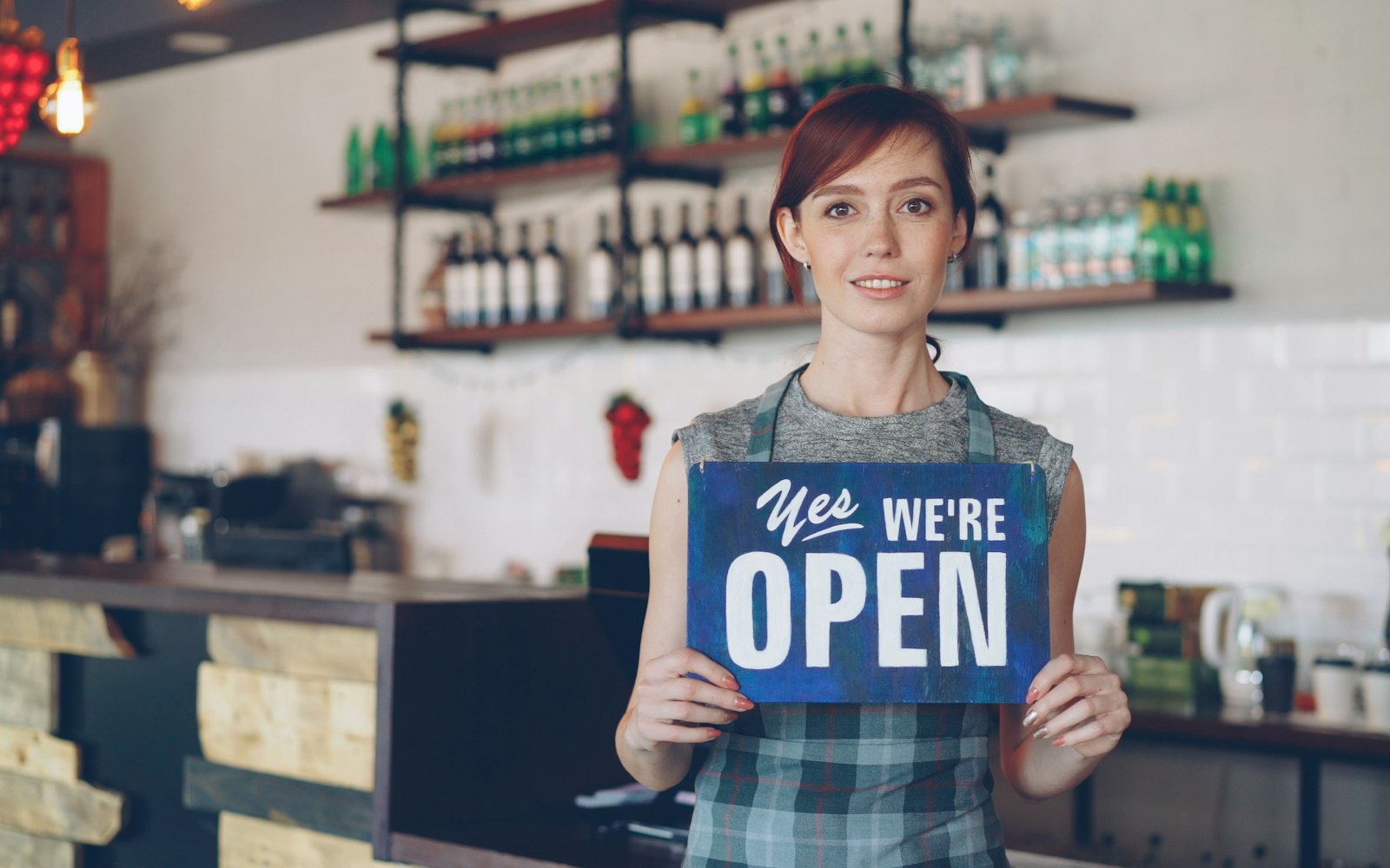 Small business owner holding an Open sign in the front window of her shop