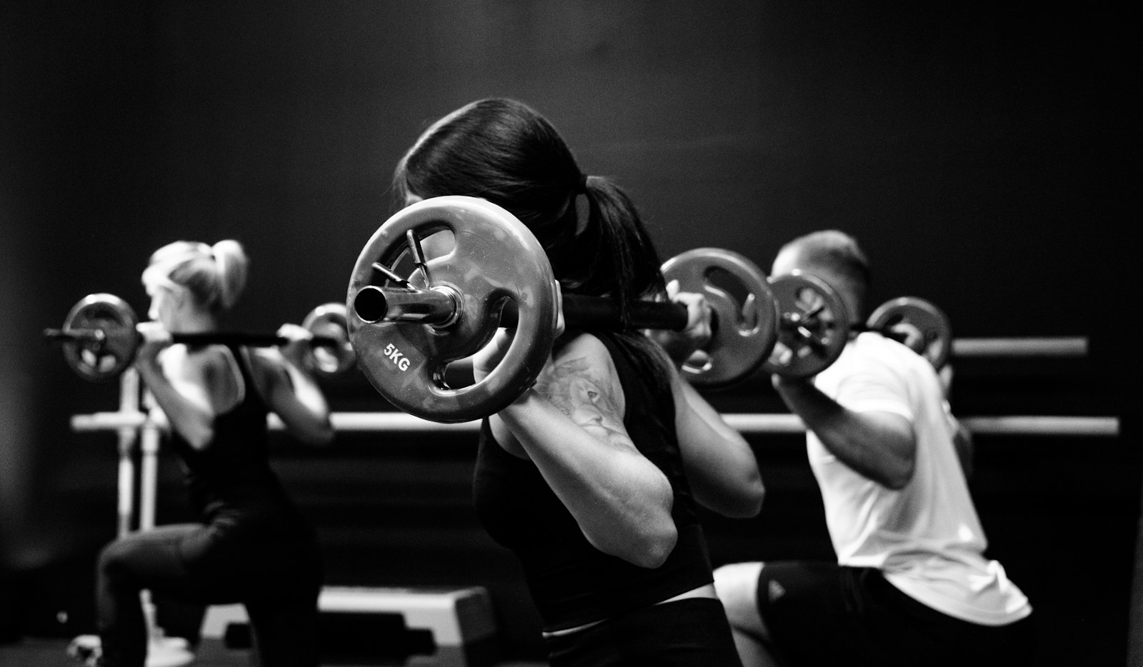 Three people lifting barbells during a strength class