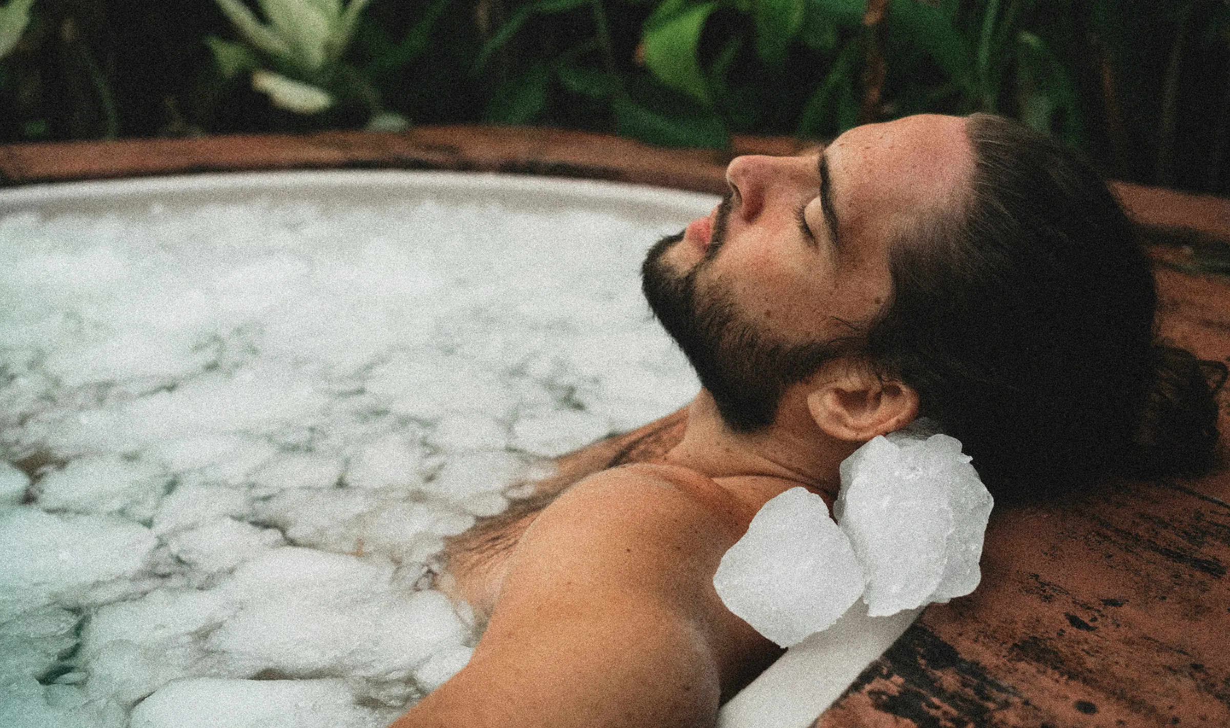 Man relaxing in a stone bath with ice on his shoulder