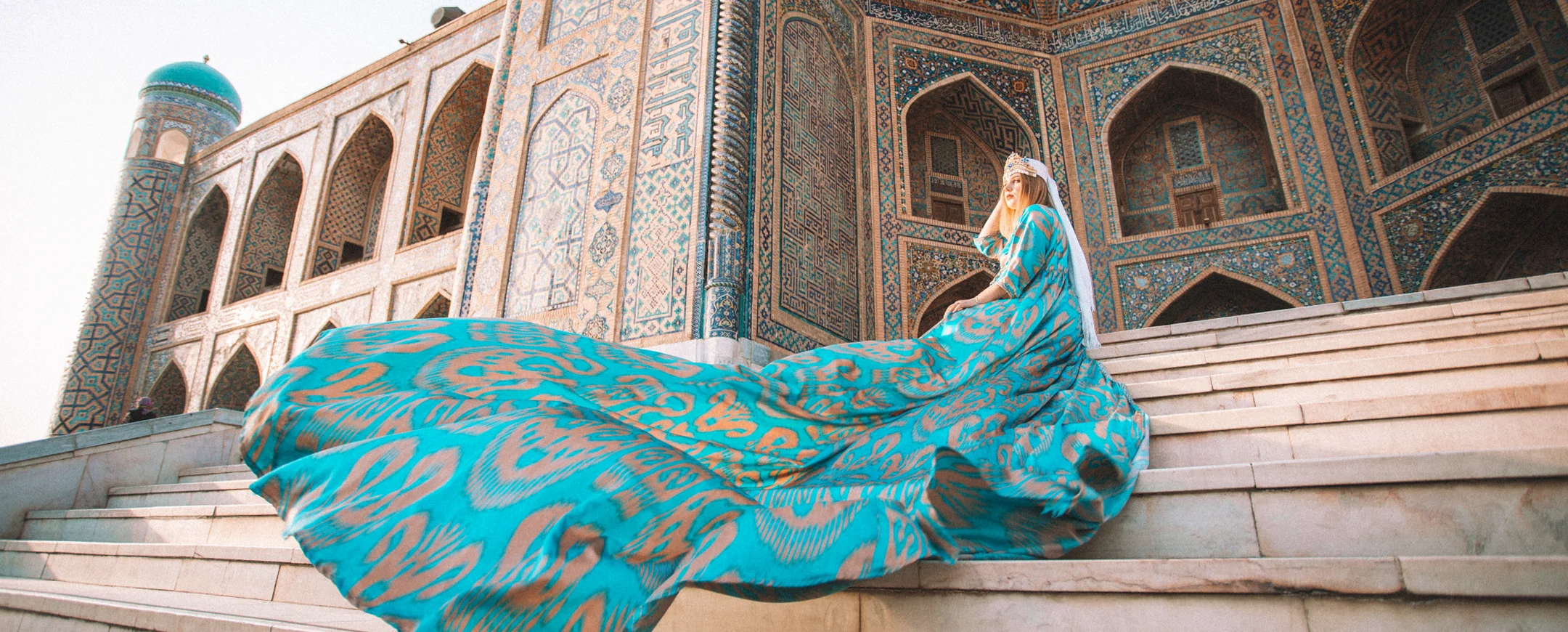 Woman in a turquoise dress on the steps of a Samarkand madrasa