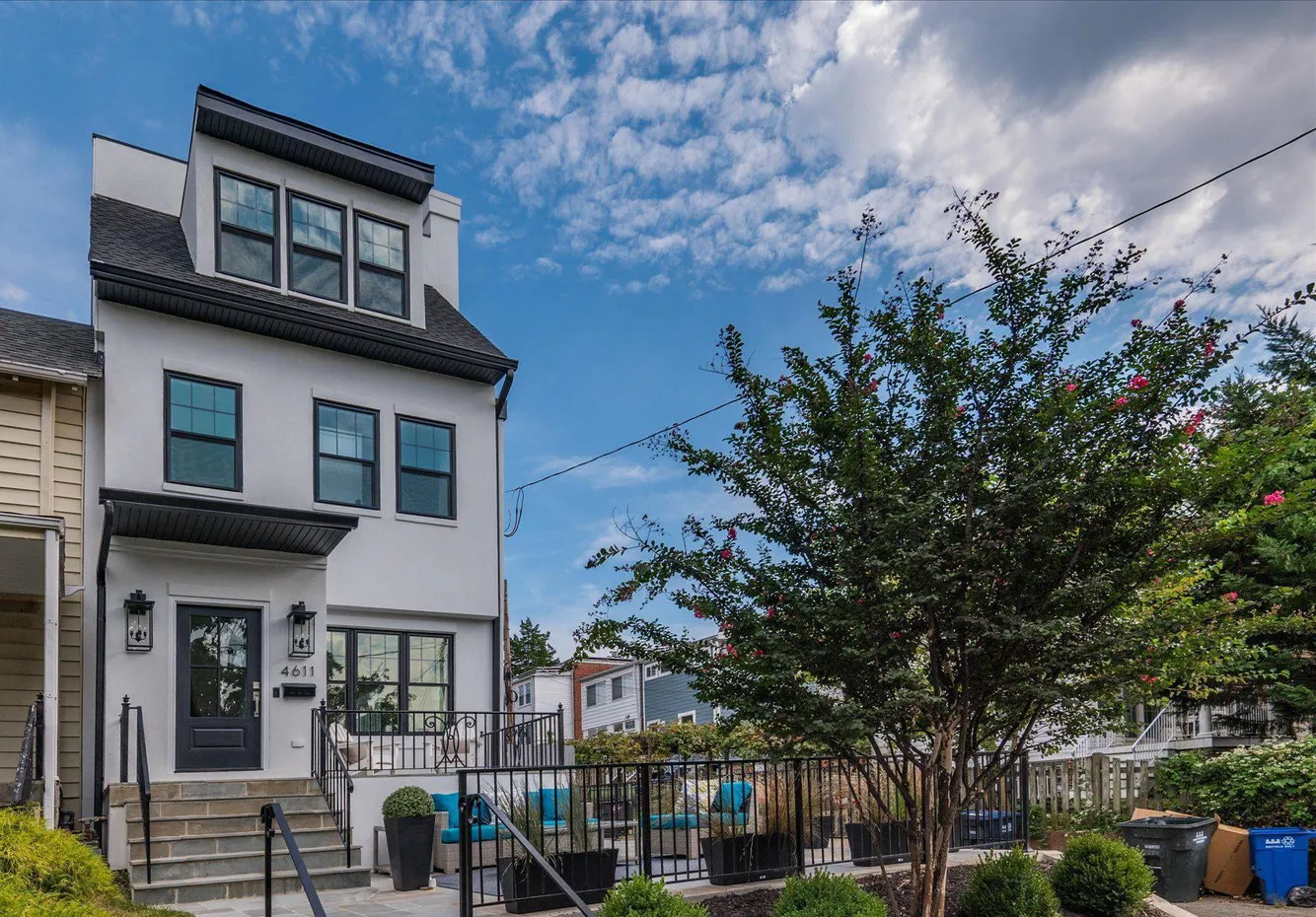 Modern white stucco townhome in Tenleytown with black-framed windows, a landscaped front terrace and a flowering tree under a blue sky