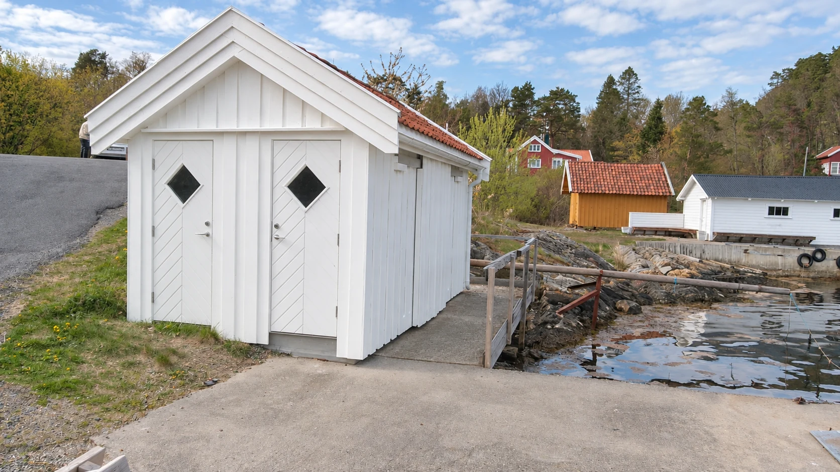 Hvitt treuthus med doble dører og rødt tegltak ved vannet