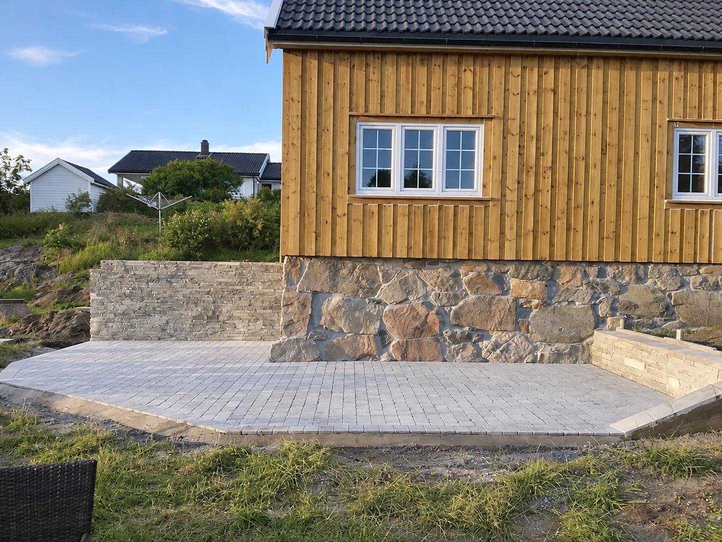 Ny uteplass i lys belegningsstein foran et tømmerkledd hus med steinmur