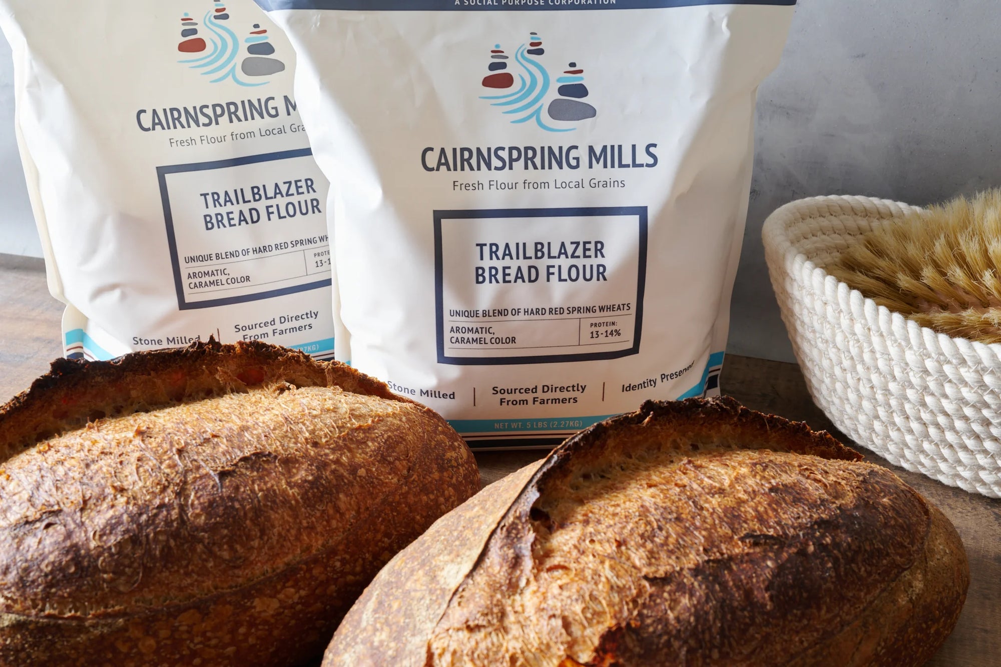 Two loaves of sourdough bread in front of bags of Cairnspring Mills Trailblazer Bread Flour