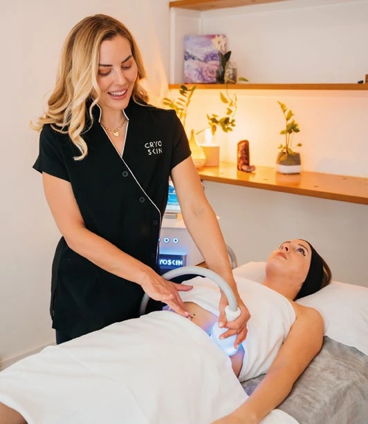 Une séance CryoSkin® : la praticienne déplace la pièce à main sur le ventre d'une cliente allongée, l'appareil à l'arrière-plan.