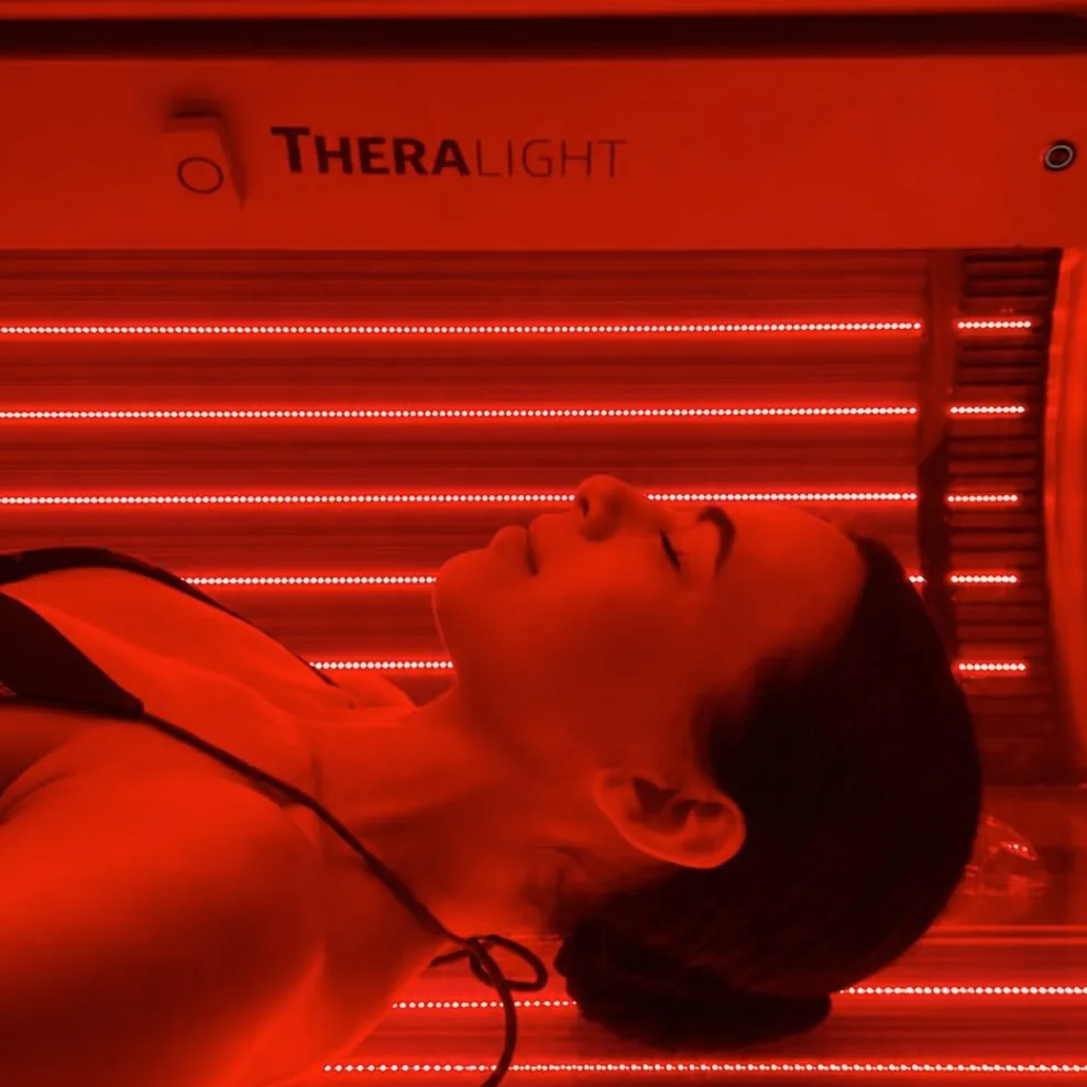 Une femme allongée les yeux fermés dans le lit de lumière rouge Theralight.