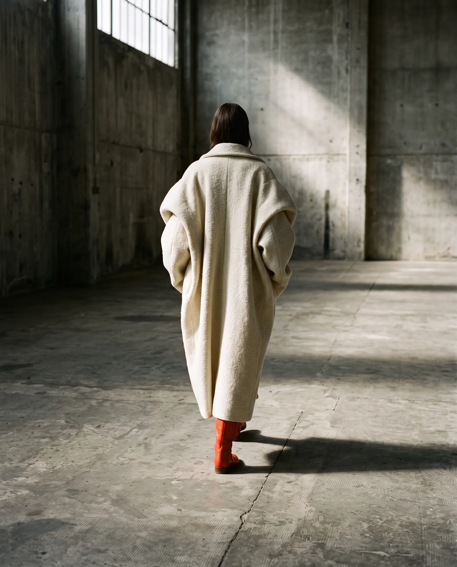 Model in a sculptural cream coat in a concrete studio