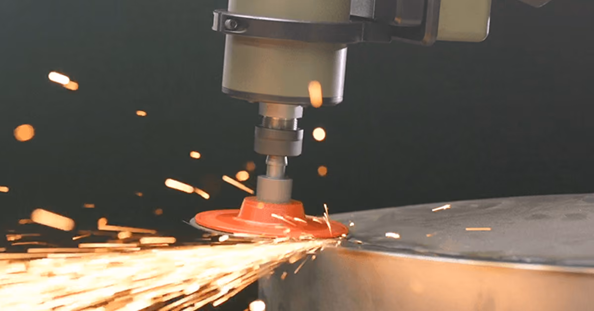 A PushCorp force-controlled grinding tool on a robot arm throwing sparks from a steel weld