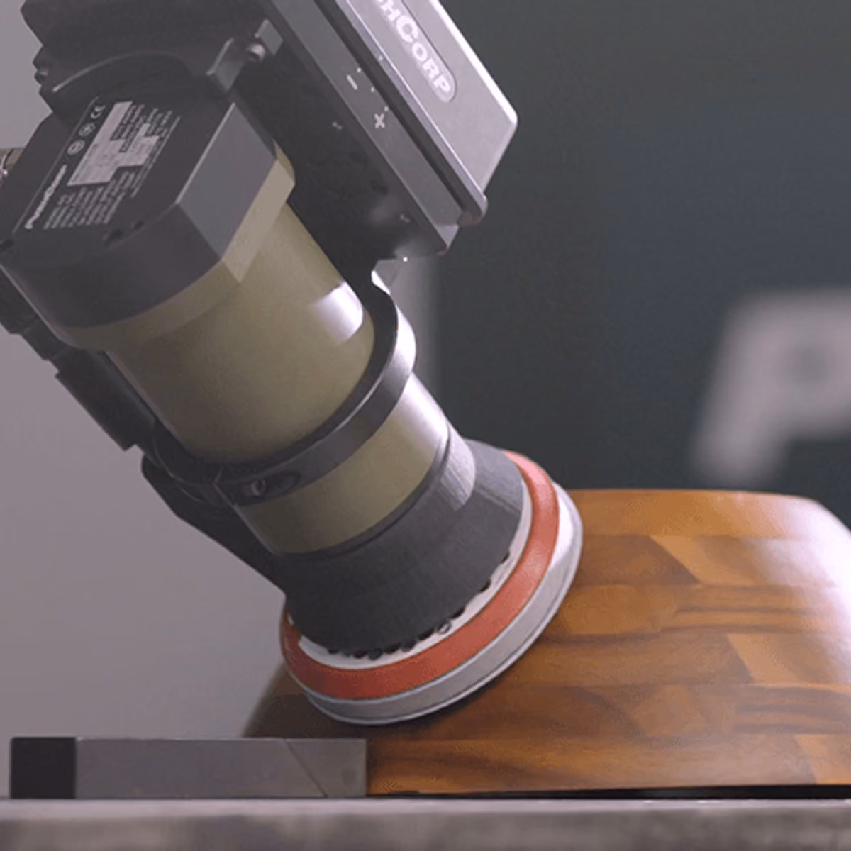 A PushCorp random orbital sander on a robot arm smoothing a curved wooden panel