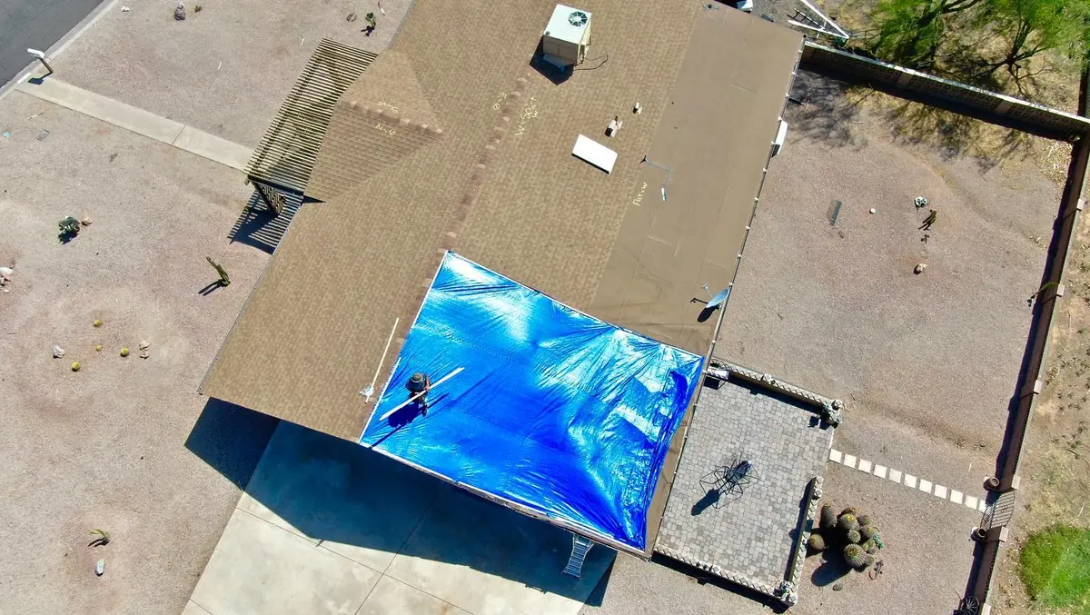 A roofer with Axis Roofing installing an Emergency Roof tarp on a shingle roof with storm damage caused by a Monsoon Storm