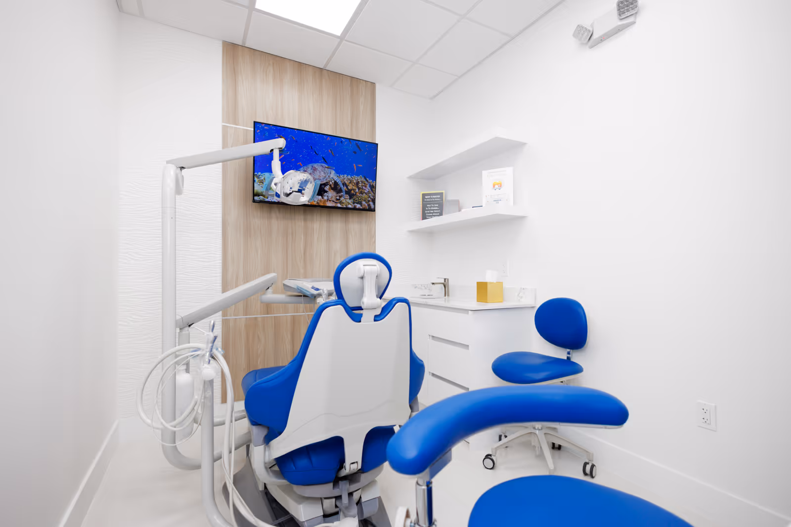 Modern dental exam room with blue patient chair, dental equipment, and TV displaying an underwater scene.